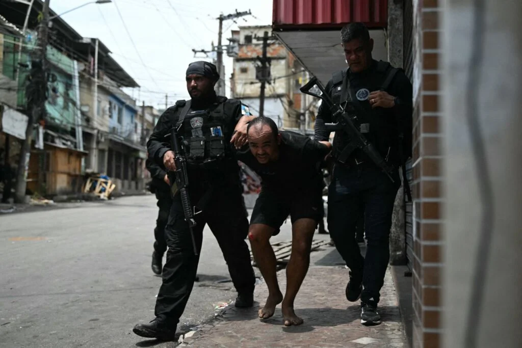 Suspeito é escoltado por policiais após ser preso durante a Operação Contenção na favela Vila Cruzeiro, no complexo da Penha, no Rio de Janeiro, Brasil, em 28 de outubro de 2025. (Foto: Mauro PIMENTEL / AFP)